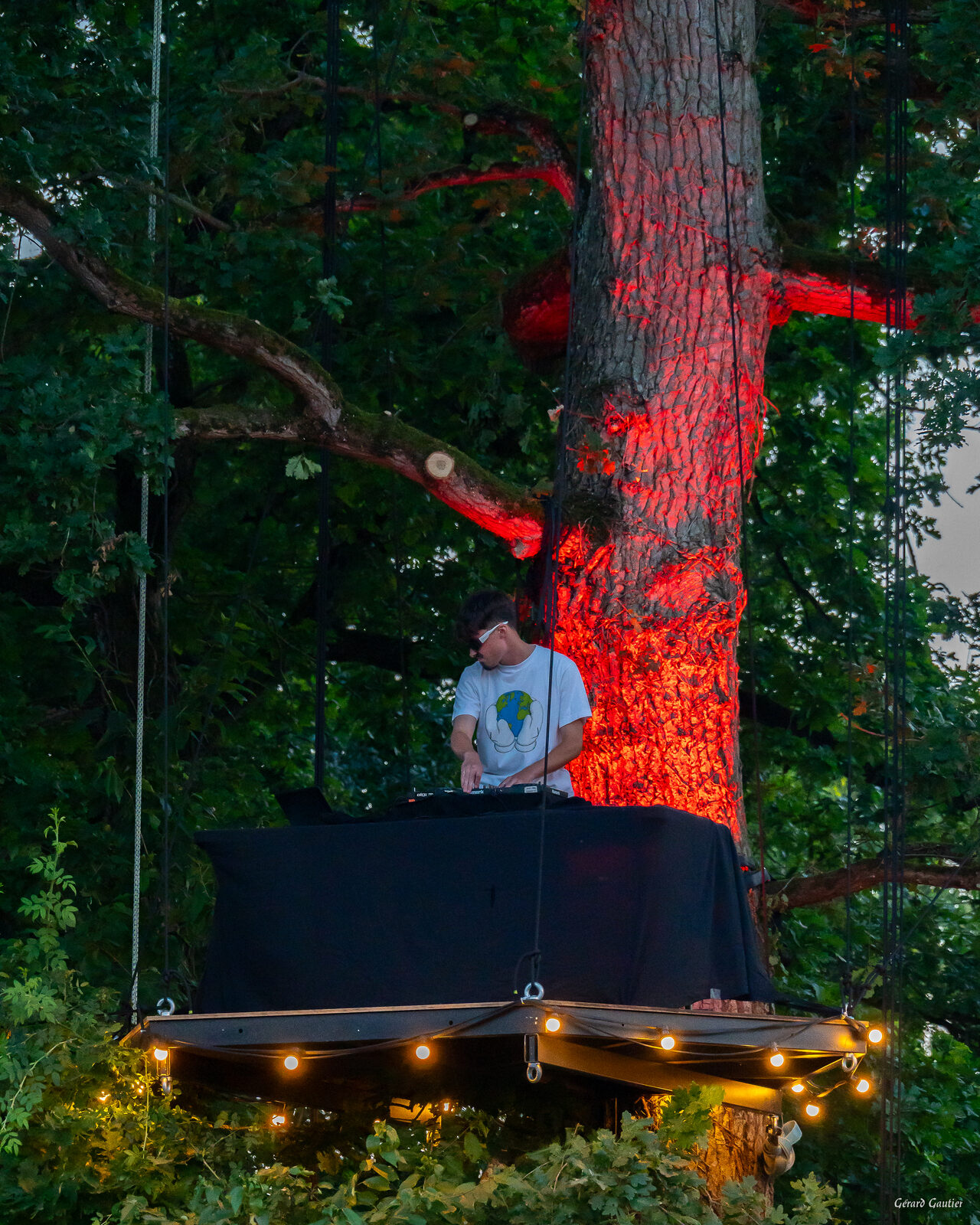 DJ set nocturne sur L'Arborium avec arbre illuminé en rouge et guirlandes lumineuses - ambiance festival de nuit en Bretagne